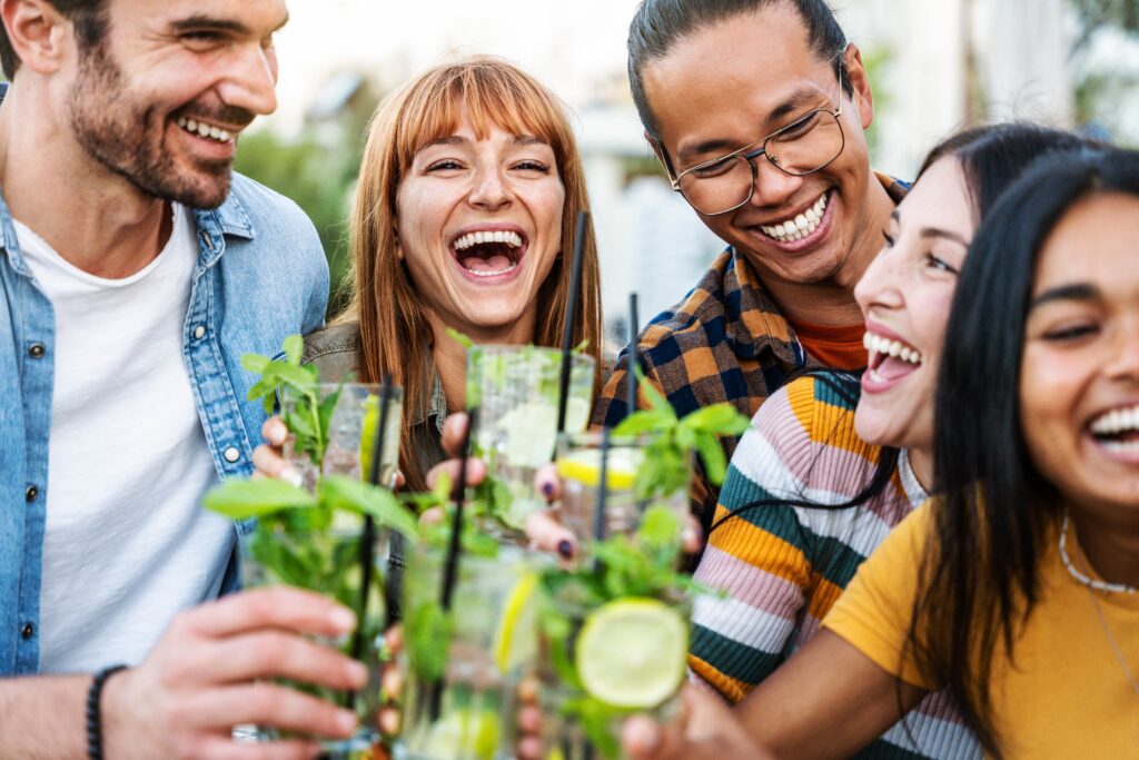 Group of friends toasting with mint drinks outdoors, smiling and laughing.