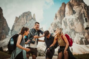 Four friends laughing together while hiking with backpacks in front of dramatic Dolomites peaks