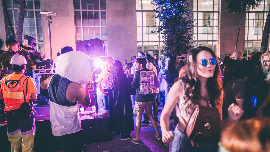 pexels-onbab-7312697 - Couchsurfing Blog A crowd in costumes, including people in panda heads, dancing at an outdoor night party near a stage with purple lighting