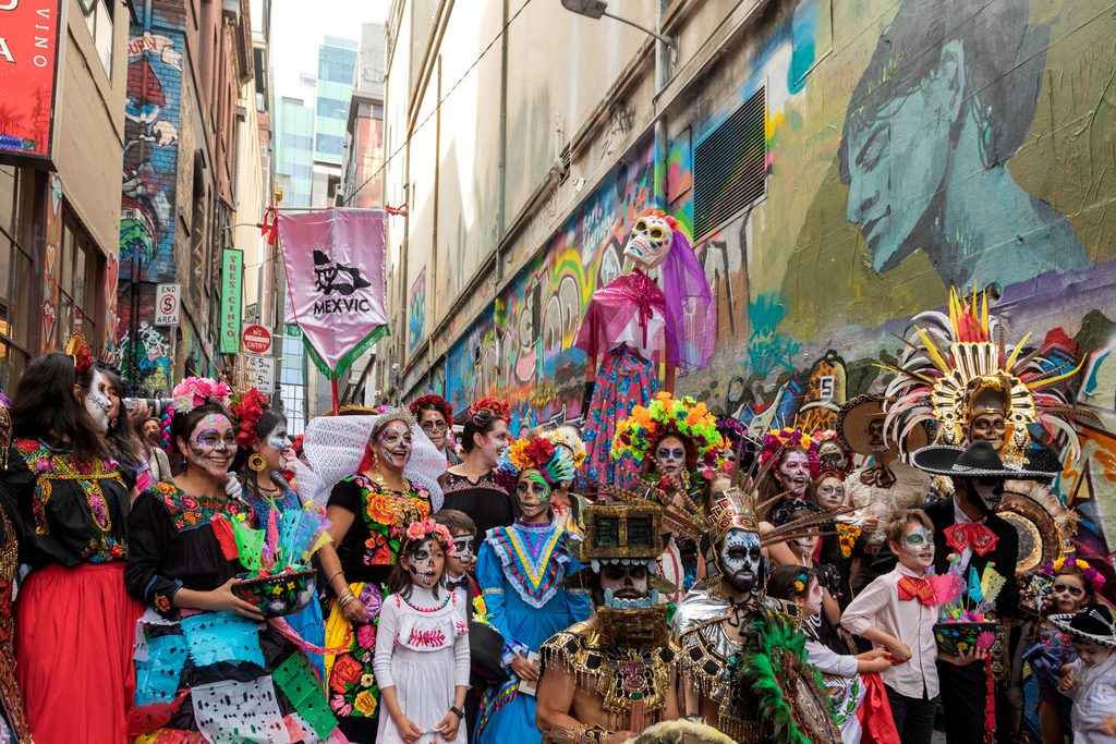 pexels-robert-stokoe-105922-29233196 - Couchsurfing Blog A crowd of adults and children in skeleton face paint, flowers, and traditional costumes gathered in a mural-covered alley