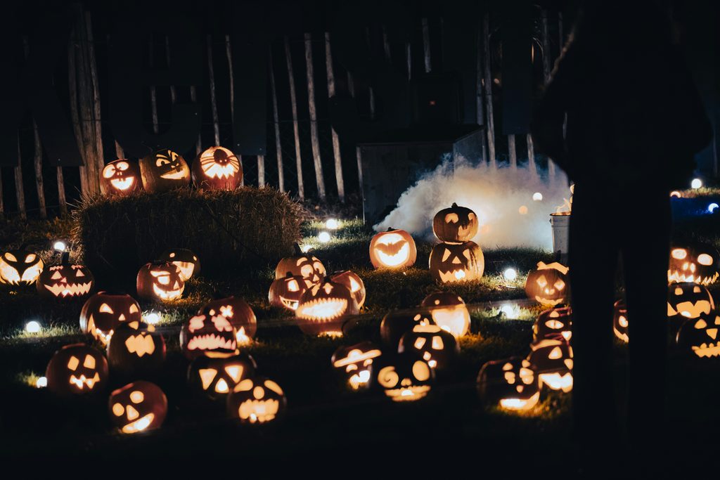 sergio-zhukov-7XdROmbao6g-unsplash - Couchsurfing Blog Dozens of glowing carved jack-o'-lanterns on grass at night, with a hay bale and mist in the background